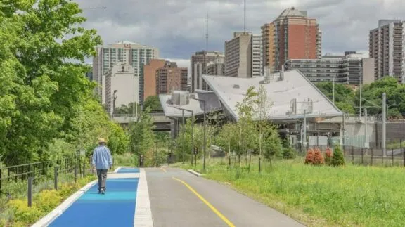 Voie cyclable et sentier piétonnier séparés avec des personnes marchant sur la voie piétonne et la station de l’O-Train Pimisi en arrière-plan.