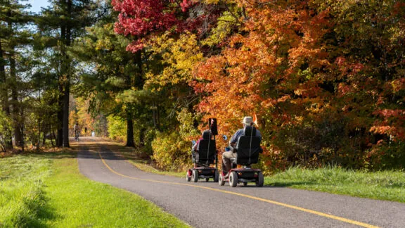 Deux personnes en quatriporteurs sur un sentier polyvalent, et un cycliste en sens inverse, à l'automne.