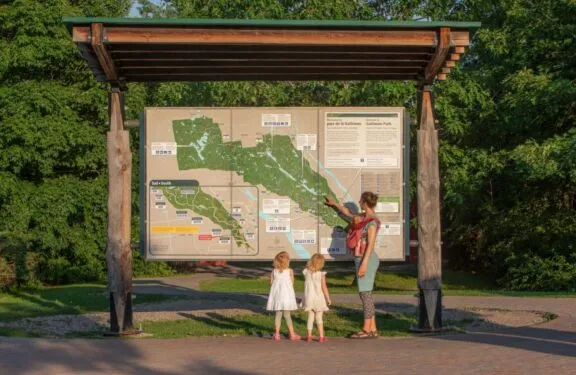 A family looks at the map of Gatineau Park on a trail.