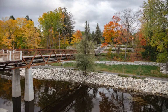 Fall scene of a truss bridge over water leading to a terraced bank.