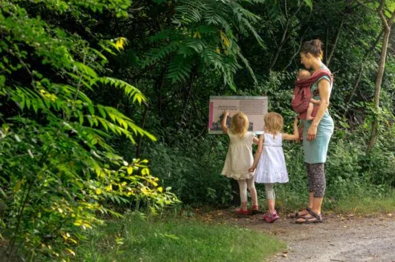 A family gathers around an interpretive sign on a hard-packed dirt trail.
