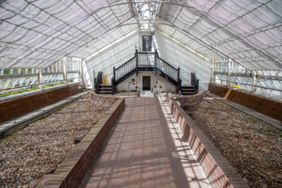 Interior of a greenhouse with empty flower beds and closed window shades.