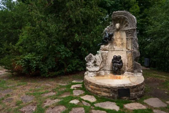 Ruins of Soper’s Fountain, still ornamented with three bronze putti, sitting on rustic paved stones and grass.