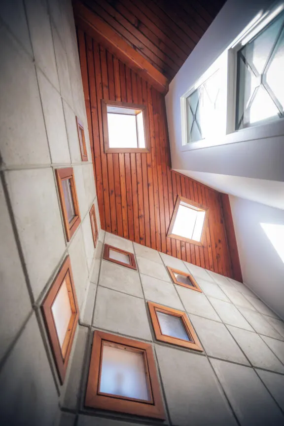Wood-slat ceiling with two skylights and a concrete wall with several frosted glass windows.