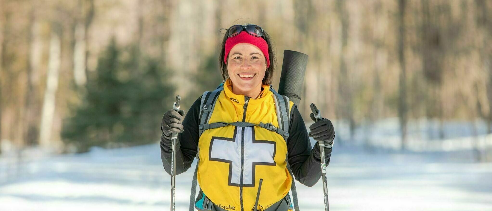 Bénévole portant une veste de premiers secours, sur un sentier de ski, face à l’appareil photo