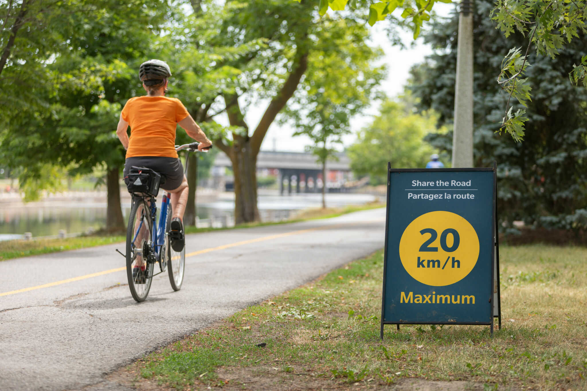 Cycliste sur le Sentier de la capitale à côté d’un écriteau sur lequel est inscrit « Partagez la route, 20 km/h maximum ».
