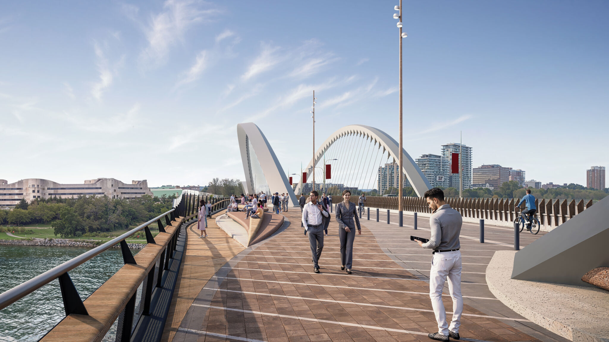 Le belvédère se trouve à gauche, l’allée piétonnière est au centre et la piste cyclable est à droite. Le belvédère possède une surface en bois avec des rampes surplombant la rivière. Le passage piétonnier au centre présente un motif en briques et est utilisé par les piétons. La piste cyclable à droite offre une surface plus lisse pour les cyclistes. Les gens marchent et font du vélo, respectivement, sur ces voies. Les bâtiments et les arcs du pont sont visibles en arrière-plan.