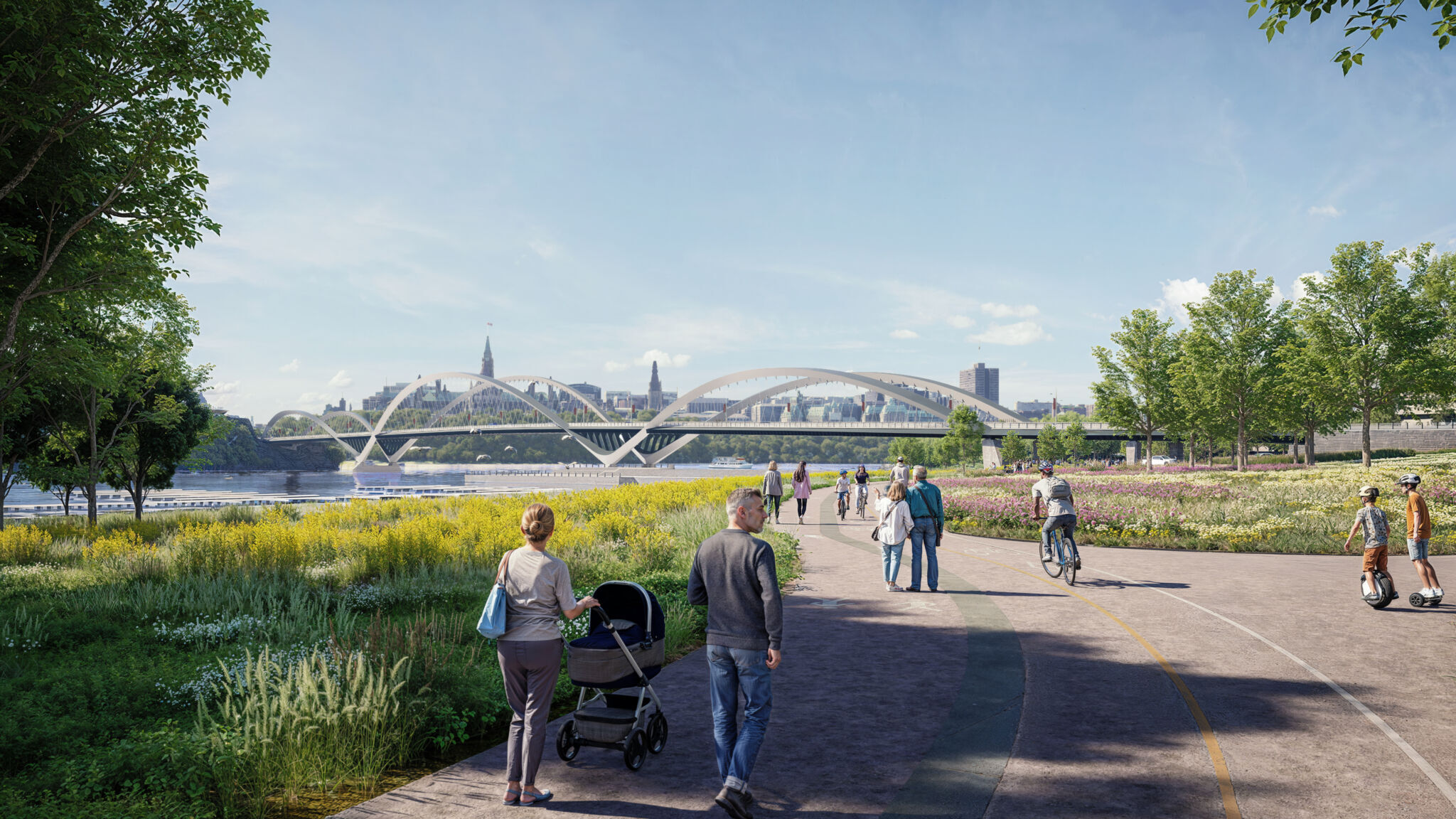 Vue de la berge et du pont depuis le parc Jacques-Cartier. À l’avant-plan, il y a un sentier pavé où les gens marchent, font du vélo et utilisent des véhicules gyroscopiques. Il y a de la verdure et des plantes à fleurs des deux côtés du sentier, ainsi que des arbres qui bordent la zone. L’horizon de la ville est visible au-delà du pont.