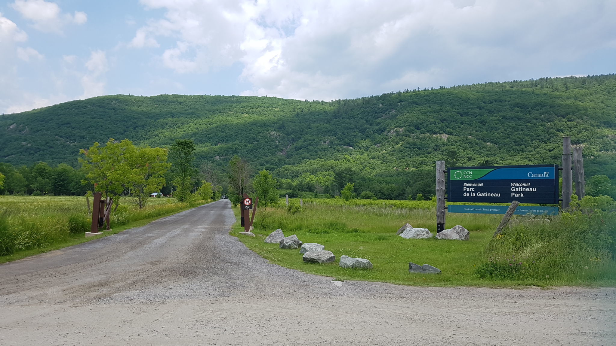 Le secteur de la chute de Luskville en été. Panneau d'accueil et route en gravier au premier plan. Les collines de l'Outaouais en arrière plan.